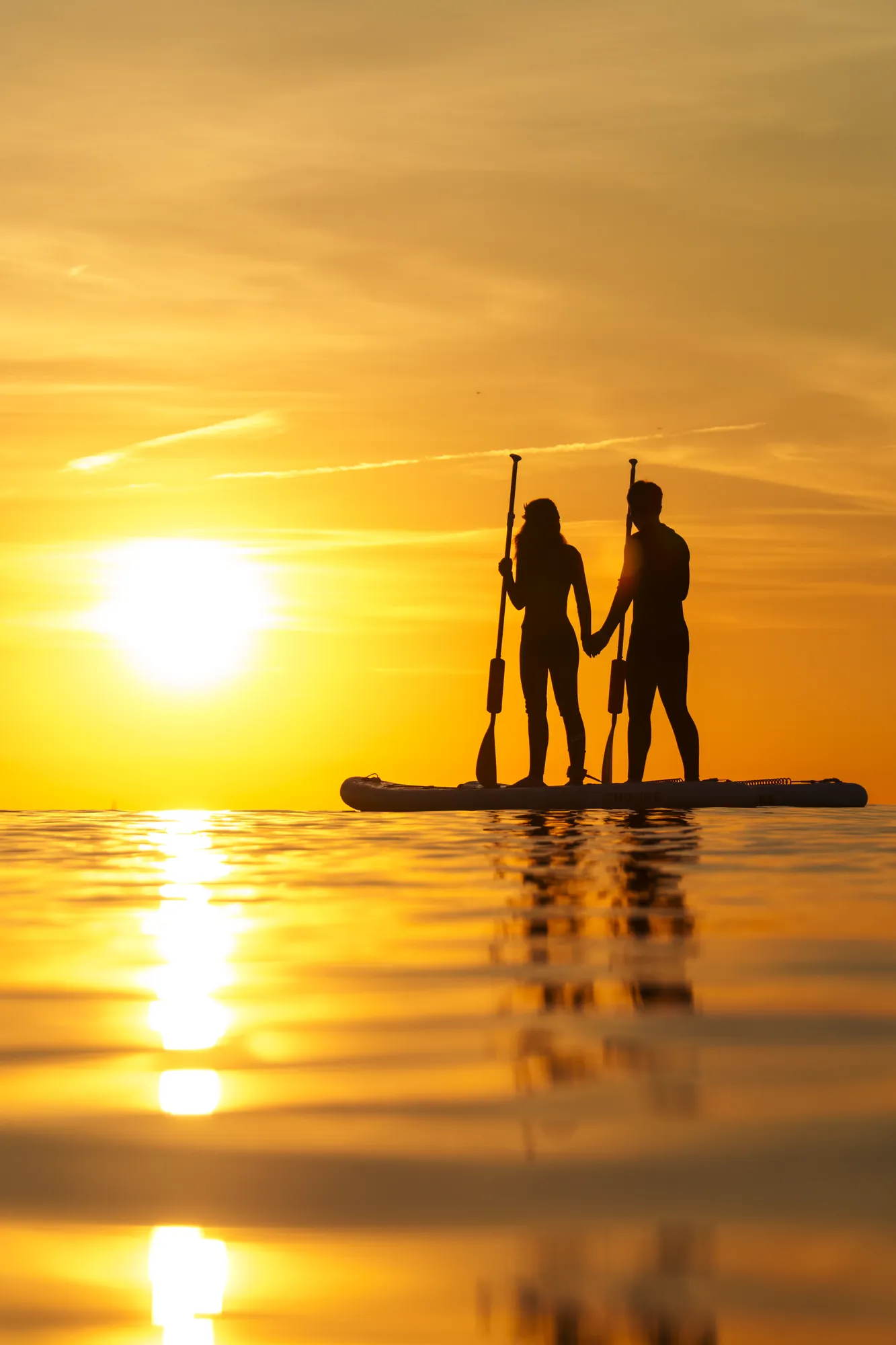 Couple on a SUP board at sunrise in Sitges, Riera Xica beach