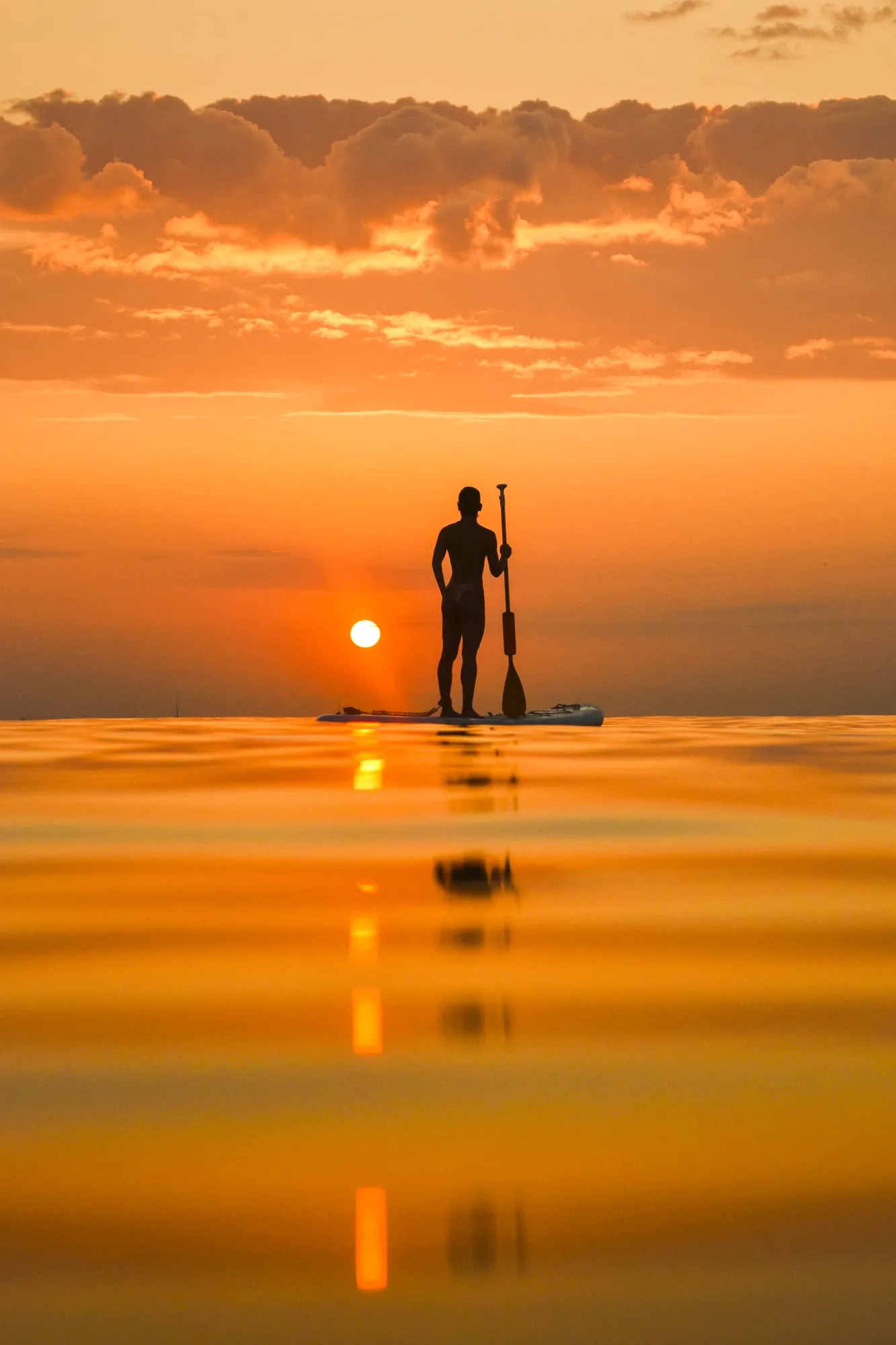Man doing stand up paddle at sunrise on the open sea in Sitges